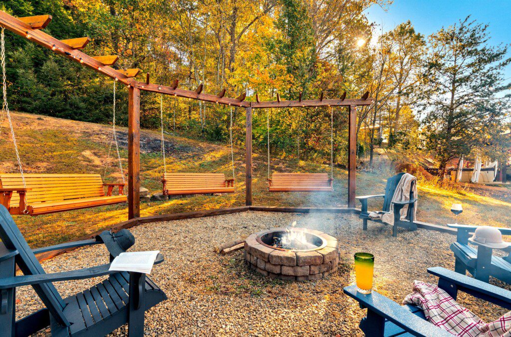 Outdoor fire pit area at Moonlit Meadows, a cabin rental in Wears Valley, with swings, chairs, and forested autumn surroundings