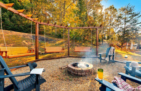 Outdoor fire pit area at Moonlit Meadows, a cabin rental in Wears Valley, with swings, chairs, and forested autumn surroundings